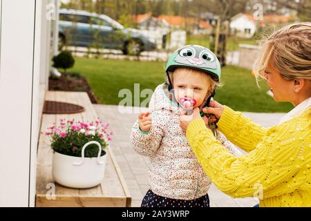 Mutter setzt ihre Töchter mit dem Fahrradhelm auf Stockfoto