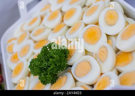 Eine ganze Reihe von gekochten, in Scheiben geschnittenen Eiern, die mit Petersilie an einem Buffet in festlicher Atmosphäre dekoriert sind Stockfoto