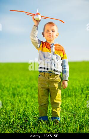 Fröhlicher Junge spielt mit Spielzeugflugzeug gegen blauen Himmel und grüne Feld Hintergrund. Stockfoto