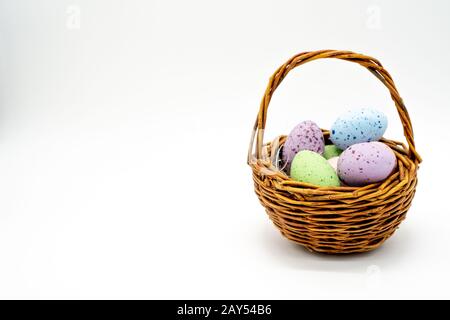 Mini gewebter osterkorb mit farbigen gesprenkelten Eiern, isoliert auf weißem Hintergrund Stockfoto