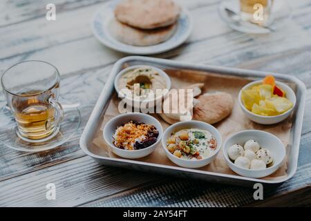 Overhead-Bild traditioneller israelischer Speisen auf dem Tablett Hummus, Hausziegenkäse, Tomatenkern, Rote Bete mit Gewürzen, Pita Brot, Getränk im Glas Stockfoto