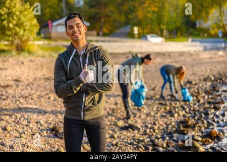 Mann zeigt Daumen hoch mit Freiwilligen am Strand Stockfoto