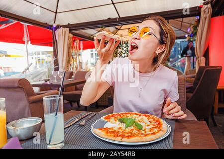 Junges Mädchen, das köstliche Pizza mit Käse und Grüns in der Pizzeria isst Stockfoto