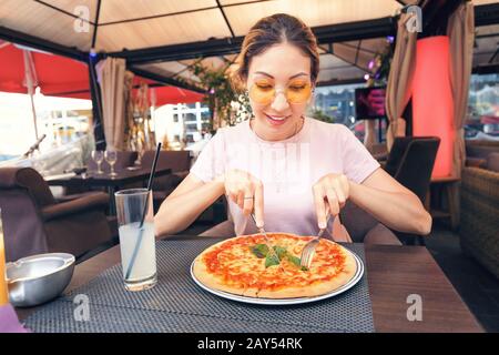 Junges Mädchen, das köstliche Pizza mit Käse und Grüns in der Pizzeria isst Stockfoto