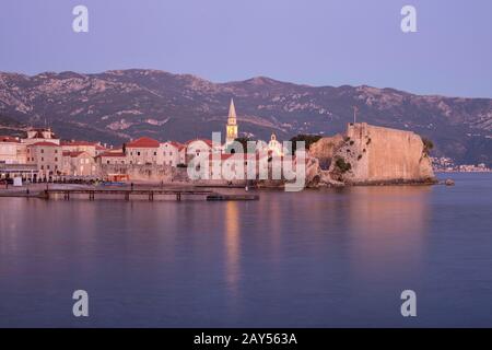 Sonnenuntergang über der Zitadelle von Budva an der Adria. Außerhalb der Stadtmauern liegt der alte Stadtstrand und Pier. Montenegro. Stockfoto