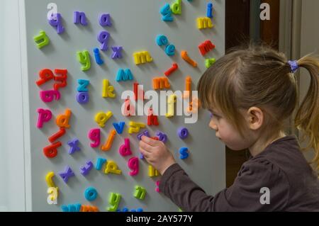 Junges Mädchen, das mit Buchstaben aus dem Kühlschrank spielt Stockfoto