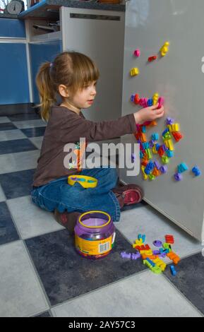 Junges Mädchen, das mit Buchstaben aus dem Kühlschrank spielt Stockfoto