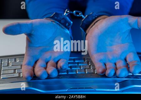 Hände eines Mannes in Handschellen auf dem Hintergrund einer Computertastatur Stockfoto