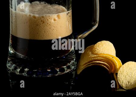 Bier in transparenten Glas- und Kartoffelchips auf schwarzem Glashintergrund. Nahaufnahme Stockfoto