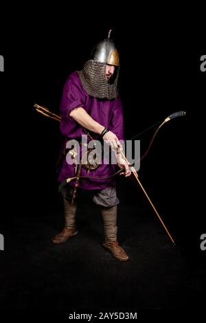 Mann im mittelalterlichen Kleid, violettes Hemd und Helm halten einen Bogen, die Ironie: Der Schrank ist ziemlich gereift Stockfoto