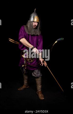 Mann im mittelalterlichen Kleid, violettes Hemd und Helm halten einen Bogen, die Ironie: Der Schrank ist ziemlich gereift Stockfoto