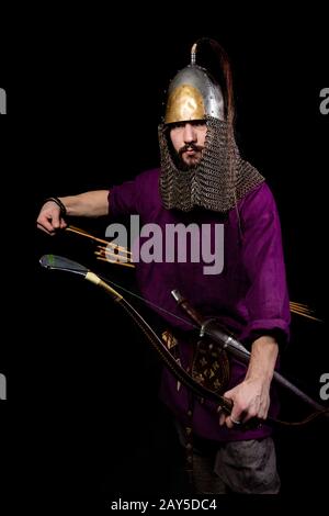 Mann im mittelalterlichen Kleid, violettes Hemd und Helm halten einen Bogen, die Ironie: Der Schrank ist ziemlich gereift Stockfoto