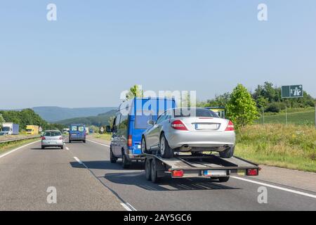 Trailer mit Auto. Blauer Kleinbus mit LKW-Transporter, der Auto auf der Autobahn transportiert. Stockfoto