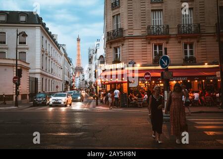 Juli 2019, Paris, Frankreich: Warmer und gemütlicher Abend in Paris mit Straßenüberquerung, kleinem Café und Eiffelturm im Hintergrund Stockfoto