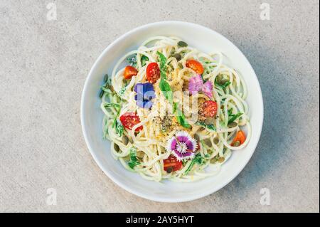 Köstlicher Zucchini-Spaghetti-Salat mit Hempsamen, Spinat, Kürbissamen, mit Blumen dekoriert, in Schüssel, isoliert über weißem Hintergrund. Essen conce Stockfoto