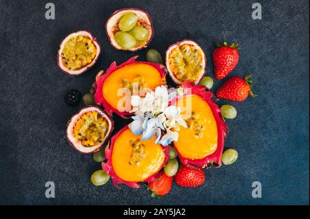 Scheiben Drachenfrucht, rote reife Erdbeere und Trauben auf dunklem Grund. Frisches Obst für veganten Salat. Ernährung und Vitamine Konz Stockfoto