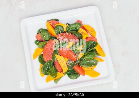 Gesundes Essverhalten und Ernährungskonzept. Frischer Mango-Salat, Grapefruit, Spinat und Hempsaat auf weißem, quadratischem Teller. Draufsicht. Organisches Gericht Stockfoto