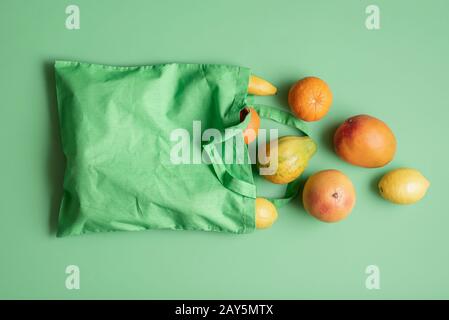 Tropische Früchte in einer grünen Stofftasche auf grünem Hintergrund. Exotische Sommerfrüchte in einer wiederverwendbaren Tasche. Frisches Obst im Sonderangebot. Lebensmittel-Shopping-Konzept. Stockfoto