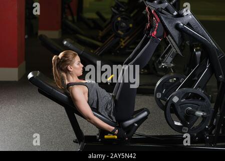 Sportliche Frau mit Gewichten-Presse-Maschine für die Beine. Fitness-Studio. Stockfoto