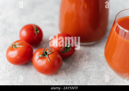 Nahaufnahme von vier reifen roten Tomaten auf weißem Hintergrund, frischer Saft in Gläsern in der Nähe. Gesunder Lebensstil. Köstliches Getränk aus Gemüse Stockfoto