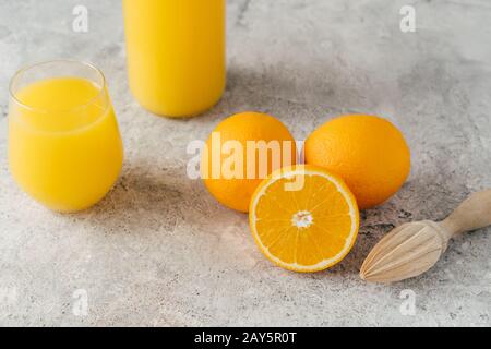 Blick auf frische Orangen und frischen Orangensaft aus Glas, Holzsafter auf weißem Tisch. Multifruchtsaft. Fruchtgetränk voll Vitamin C Stockfoto