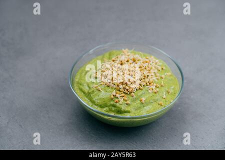 Schüssel aus grünem Smoothie aus Spinat mit Buchweizensprossen auf grauem Grund. Veganes Essen. Gesundes Essverhalten und Ernährungskonzept Stockfoto