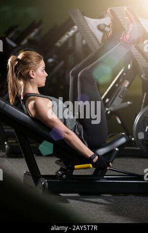 Sportliche Frau mit Gewichten-Presse-Maschine für die Beine. Fitness-Studio. Stockfoto