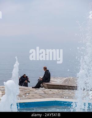 Athen, Griechenland - 26. Januar 2020: Ein Mann blickt auf das Meer und ein küßendes Paar in Paleo Faliro an einem nebligen Tag Stockfoto