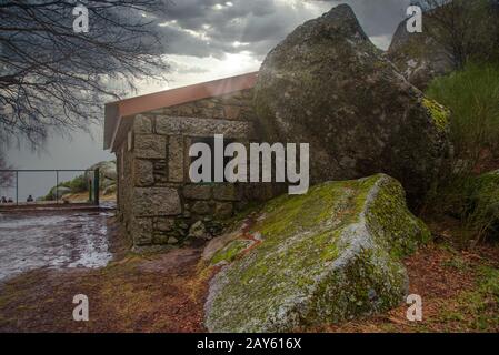 Kleine Steinhütte, gebaut zwischen moosbedeckten Felsbrocken in Serra da Estrela, Portugal, unter einem dramatisch bewölkten Himmel Stockfoto