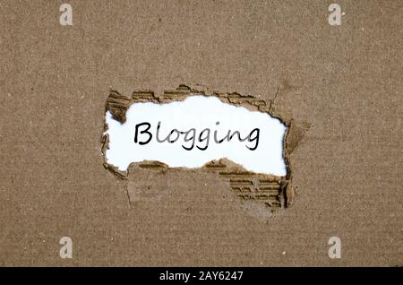 Das Wort Blogging erscheint hinter zerrissenes Papier Stockfoto