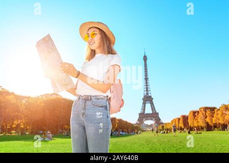 Fröhliche asiatin, die die Karte vor dem berühmten Pariser Wahrzeichen - dem Eiffelturm - liest. Tourismus in Frankreich Stockfoto