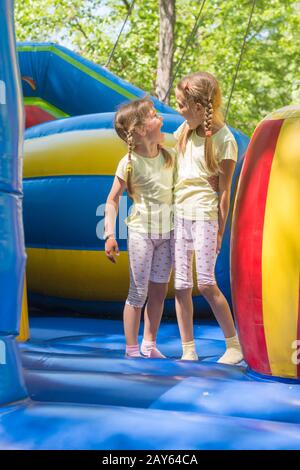 Zwei Mädchen verzog das Gesicht glücklich aussehende einander durch einen Sprung auf ein aufblasbares Trampolin Stockfoto