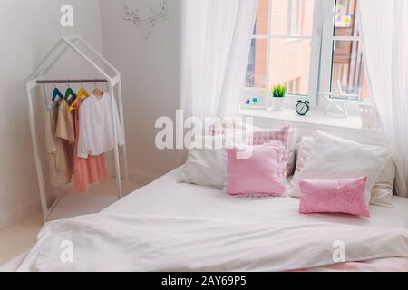 Foto von leerem, gemütlichem, geräumigen Schlafzimmer mit großem Bett, Kleidung auf Bügeln, Fenster mit weißen Vorhängen. Häusliche Atmosphäre. Innenschuss Stockfoto