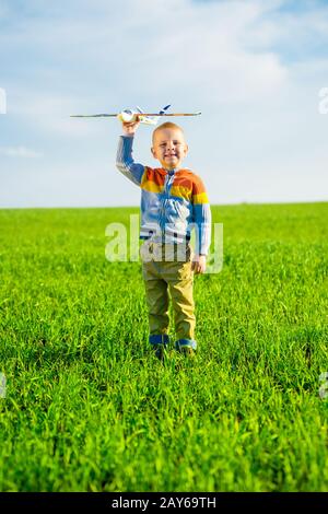 Fröhlicher Junge spielt mit Spielzeugflugzeug gegen blauen Himmel und grüne Feld Hintergrund. Stockfoto