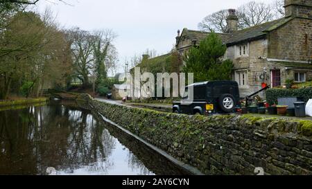 Land Rover Defender unterwegs und auf der Landstraße vorbei an malerischen Häusern und historischem Mühlenteich - Embsay Village, North Yorkshire, England, Großbritannien. Stockfoto