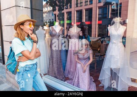 Eine glückliche asiatische Frau, die im Schaufenster eines Ladens Hochzeit oder Abendkleid auswählt Stockfoto