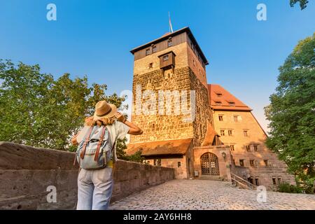 Touristenmädchen mit Blick auf den hohen Turm der Kaiserlichen Burg Nürnberg bei Sonnenuntergang Stockfoto