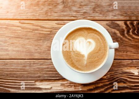 Cappuccino-Kaffeetasse mit herzförmigem Schaum auf einem Holztisch im Café Stockfoto