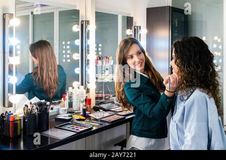 Professionelle Make-Up-Künstlerin, die einem schönen jungen Mädchen Make-up in die niedliche Studie macht Stockfoto