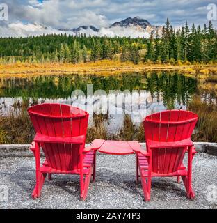 Zwei rote Kunststoffstühle, miteinander verbunden, befinden sich am See Stockfoto