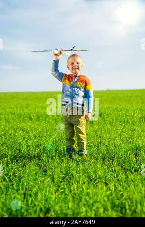 Fröhlicher Junge spielt mit Spielzeugflugzeug gegen blauen Himmel und grüne Feld Hintergrund. Stockfoto