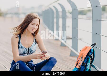 Positive Fitness Mädchen in der Oberseite und Leggings, hat einen guten Ausdruck, wie liest angenehme Textnachricht von Freund, hat dunkle Haare, ruht im Freien. P Stockfoto