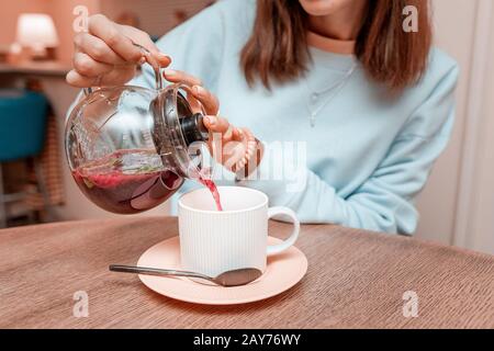 Das Mädchen gießt aus dem Wasserkocher in einen Becher duftenden roten Früchtetee Stockfoto