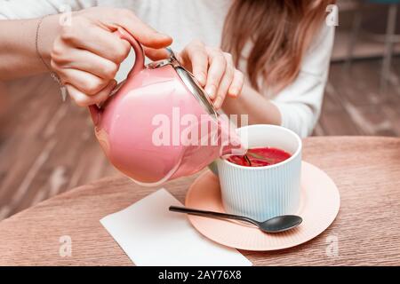 Das Mädchen gießt aus dem Wasserkocher in einen Becher duftenden roten Früchtetee Stockfoto