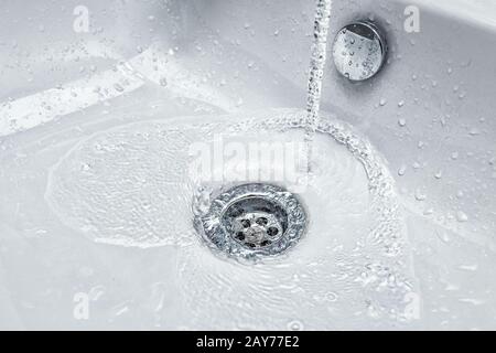 Ein Wasserstrahl strömt in die Spüle, das Konzept von Abwasser und Umweltproblemen Stockfoto