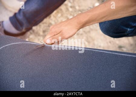 Boy schneidet das Griptape auf einem Skateboard Stockfoto