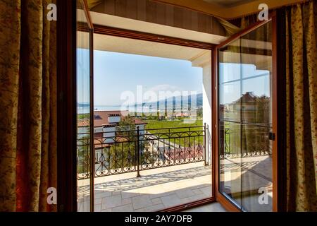 Die offene Tür zur Veranda einer Luxuskabine mit Blick auf die Berge und das Meer. Glastür mit Holzrahmen, dunkle Vorhänge. Novorossijsk Stockfoto