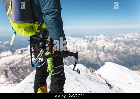 Nahaufnahme EIN junger Kerlkletterer hält in der Hand eine Eisaxt, die auf einem Gipfel hoch in den Bergen steht. Extremes Sportkonzept Stockfoto