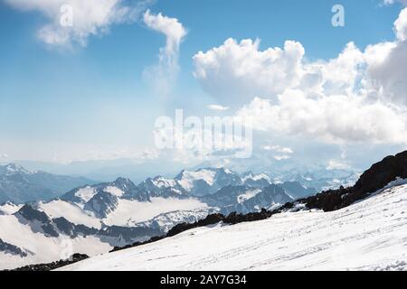 Dunkelblauer Himmel mit Wolken auf den felsigen Gipfeln der Berge, die von Gletschern und Schnee bedeckt sind Stockfoto