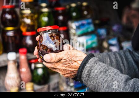 Alte, zerknitterte weibliche Hände halten den Mixbecher mit Stau Stockfoto